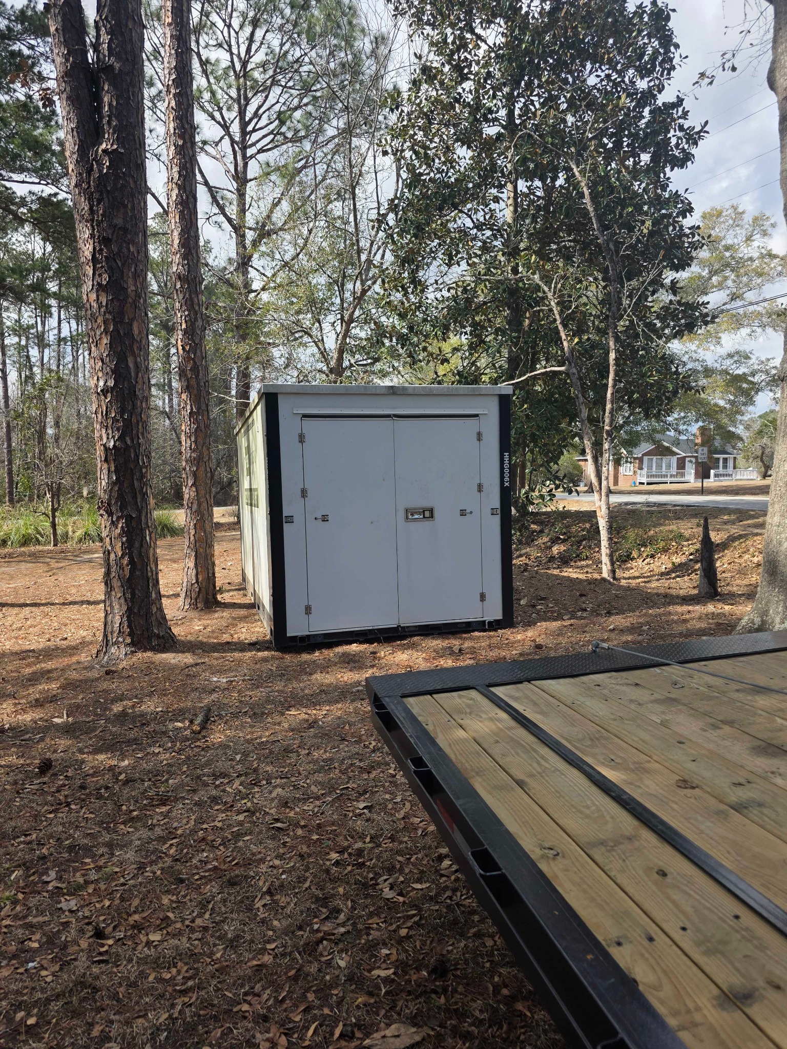 White storage container placed among pine trees near a driveway